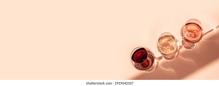 Glasses of red, rose and white wine with sunshine shadow effect. Concept of wine tasting. Flat lay, top view, copy space. Banner.