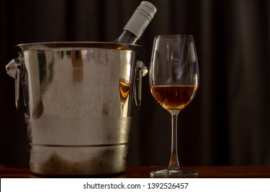 A Glasses Of Rose Wine On Wooden Table With A Bottle In Wine Chiller Bucket To Celebrate With Dark Background In The House.