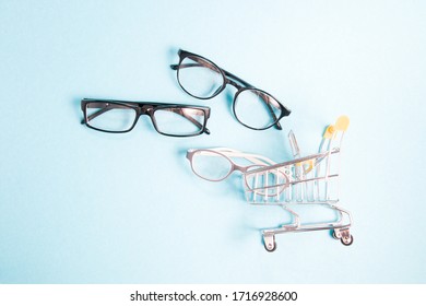 glasses for sight and a little shopping trolley, blue background, copy space, online purchase of glasses and frames for glasses, online optics store, children's glasses