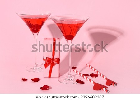 Glasses of tasty cocktail with gift and rose petals on pink background. Valentine's Day celebration