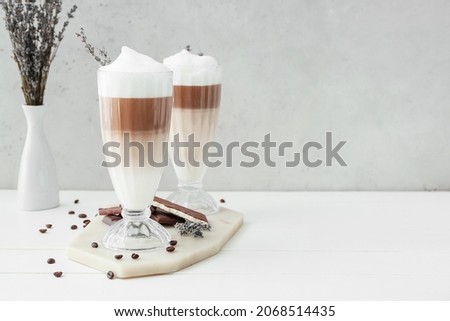 Glasses of tasty lavender latte, chocolate and flowers on light background