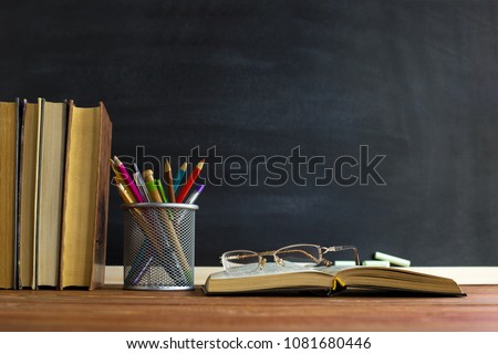 Glasses teacher books and a stand with pencils on the table, on the background of a blackboard with chalk. The concept of the teacher's day. Copy space.