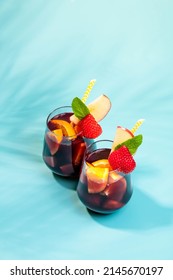 Glasses with traditional Sangria cocktail decorated with pieces of fresh strawberry, pinch of mint and eco-paper straw.
