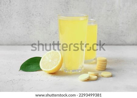 Glasses of vitamin C effervescent tablet dissolved in water and lemon on white grunge table