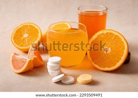 Glasses of vitamin C effervescent tablet dissolved in water and fruits on grey grunge table