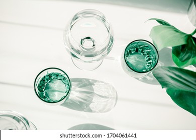 Glasses of water on white table. Harsh light through glasses, shadows. Clean minimalist contemporary art. Conceptual image. Green and white clean colors. Pure water in glass. Simple visual concept. - Powered by Shutterstock