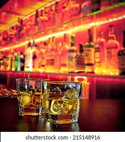 Glasses Of Whiskey With Ice On Bar Table Near Whiskey Bottle On Warm Atmosphere Lounge Bar Concept