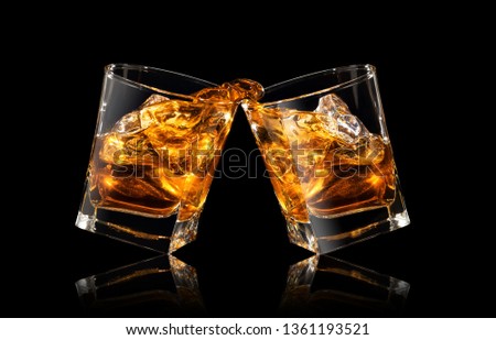glasses of whiskey making toast with splashes on black background