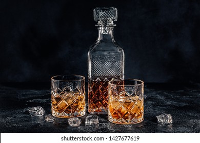 Glasses Of The Whiskey With A Square Decanter On A Black Stone Background.