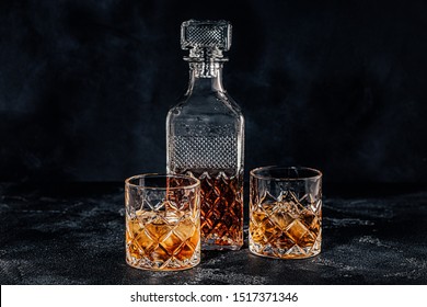 Glasses Of The Whiskey With A Square Decanter On A Black Stone Background.