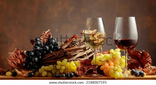 Glasses of white and red wine with bunches of\
grapes on wooden table. Copy\
space.