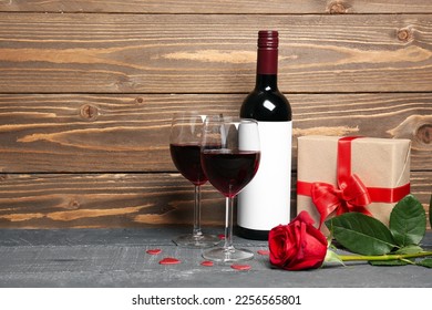 Glasses of wine, bottle, rose flower and gift box on table near wooden wall. Valentine's Day celebration - Powered by Shutterstock