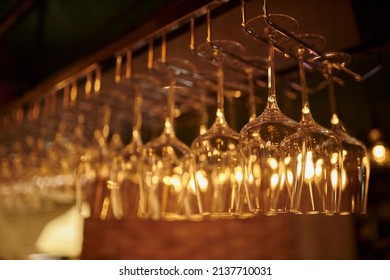 Glasses Of Wine. Glasses Hanging Above The Bar In The Restaurant. Empty Glasses For Wine. Wine And Martini Glasses In Shelf Above A Bar Rack In Restaurant. Night Life