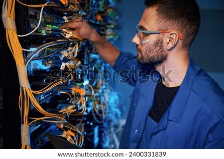 In glasses. Young man is working with internet equipment and wires in server room.