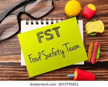 Glasses,food toys and notebook with text FST food safety team on a wooden background.