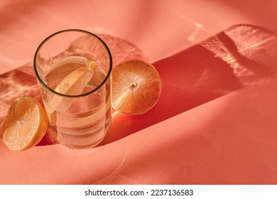 glassful of water with lemon close-up on a coral color background. Shadows and copy space. Top view - Powered by Shutterstock