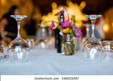 Glassware rests upside down on a white table cloth at the start of a festive dinner party in summer.