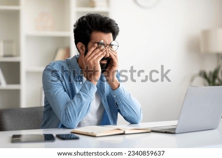 Glaucoma Concept. Young Indian Man Massaging Tired Eyes After Working On Laptop Computer, Millennial Eastern Male Suffering From Eyestrain And Fatigue, Sitting At Workplace In Home Office