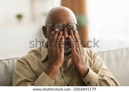 Glaucoma. Senior African American Man Rubbing Tired Eyes Wearing Eyeglasses Having Poor Eyesight Sitting On Couch At Home. Ophtalmology Diseases, Health Problems In Older Age Concept Stock foto © 