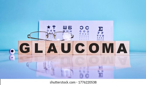 GLAUCOMA Word Written On A Wooden Cubes, Glasses, Eyes On The Background Of An Eye Test Table. Medicine Concept. Selective Focus.