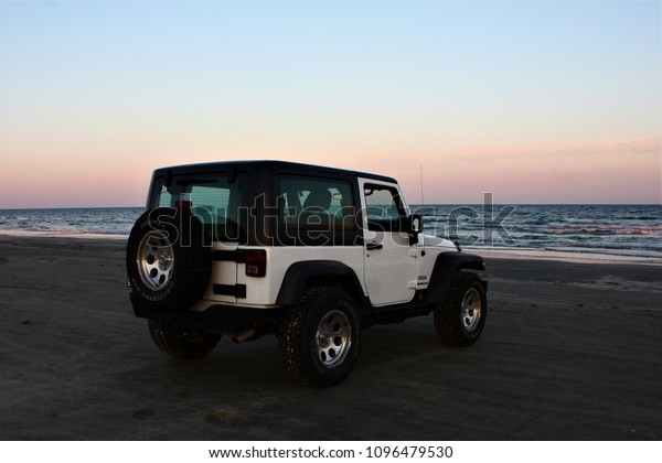 Glavestion,Texas,USA,May,9,2018: White Jeep\
Wrangler on the beach at sunset.  Empty space for text, quote, or\
saying on sky\
background.