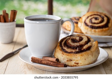 Glazed cinnamon roll and cup of coffee on a plate by a window