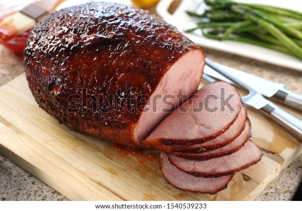 Glazed ham on wood cutting\
board.