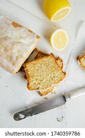 Glazed lemon pound cake loaf with poppy seed and lemon zest on a white rustic wooden table. Top view