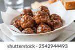 Glazed Meatballs: A bowl of glazed meatballs on a white napkin, with a slice of bread and a blurred glass of water in the background, creating a cozy, inviting scene.