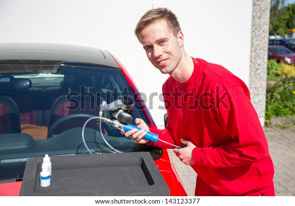 Glazier repairing windshield on a car after\
stone-chipping damage