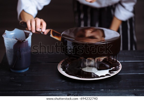 Glazing chocolate mousse cake,\
close-up. On a wooden table. Liquid chocolate\
coating