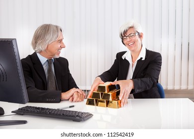 Gleeful Businesswoman Grabbing Hold Of A Stack Of Gold Bullion Bars As She Reaps The Rewards For Astute Business Practices And Investments