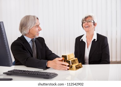 Gleeful Businesswoman Grabbing Hold Of A Stack Of Gold Bullion Bars As She Reaps The Rewards For Astute Business Practices And Investments