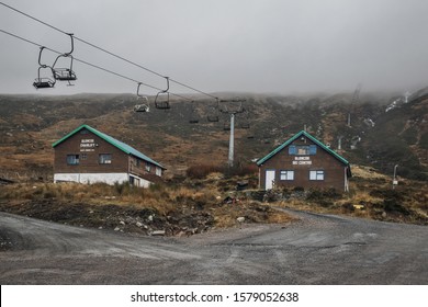 Glen Coe, Scotland -  November 25, 2019: Huts And Ski Lift In Glen Coe Ski Centre With No Snow On The Hills Covered In Dense Fog.