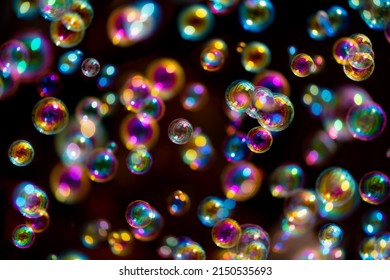 Gliding colorful bubbles isolated on black background with reflections. Soap bubbles are an extremely thin film enclosing air that forms a hollow sphere with an iridescent surface, partially blurred.