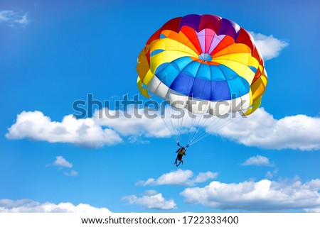 Gliding using a parachute on the background of cloudy blue sky.