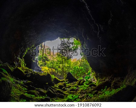 Glimpse of a male hiker watching the jungle from inside a waterfall cave