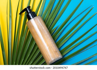 Glitter Fake Tanning Cream On Light Blue And Blue Background With Green Palm Leaf