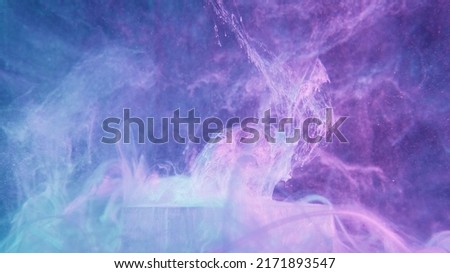 Glitter fluid splash. Neon mist texture. Fantasy explosion. Fluorescent glowing purple blue color shiny ink water splatter over ice cube on vapor cloud abstract background.
