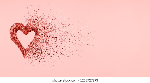 Glitter heart dissolving into pieces on pink background.  Valentines day, broken heart and love emergence concept. Horizontal wide screen banner format. Living coral theme - color of the year 2019