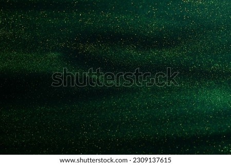 Glittering flows of gold particles in green fluid. Various stains and overflows of gold particles in liquid. Abstract shimmering background with flows of golden glitters dust.