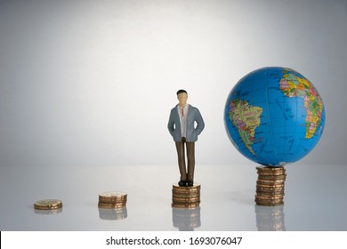 Global Capitalism Economy Lead By Successful Entrepreneur. Globe, Business Man Maniature On Top Of Stacked Coins.  Capitalism