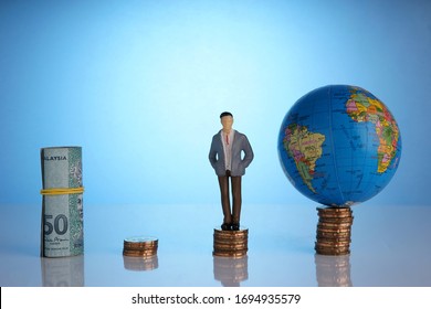 Global Capitalism Economy Lead By Successful Entrepreneur. Globe, Business Man Maniature On Top Of Stacked Coins.  Capitalism