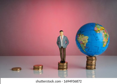 Global Capitalism Economy Lead By Successful Entrepreneur. Globe, Business Man Maniature On Top Of Stacked Coins.  Capitalism