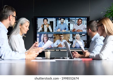 Global corporation online videoconference in meeting room with diverse people sitting in modern office and multicultural multiethnic colleagues on big screen monitor. Business technologies concept. - Shutterstock ID 1998552674