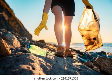 Global environmental pollution. A volunteer collects plastic bottles on the ocean shore. Legs close-up. Cleaning of the coastal zone. The concept of environmental conservation.