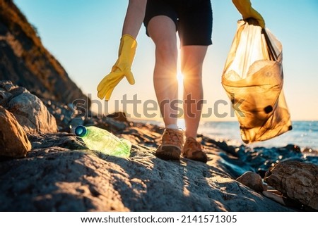 Global environmental pollution. A volunteer collects plastic bottles on the ocean shore. Legs close-up. Cleaning of the coastal zone. The concept of environmental conservation.