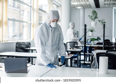 Global Epidemic Of Covid-19 And Disinfection Of Office For Return To Work Of Workers. People In Hazmat Suits, Goggles And Masks Cleaning Furniture In Interior, Copy Space