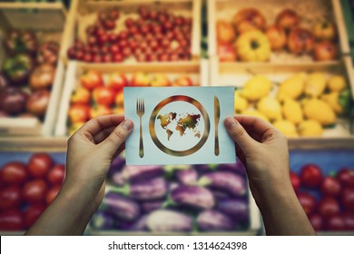 Global hunger issue, food supply problem. Hands holds a paper message as world map in a plate with knife and fork over market shelves. International starvation metaphor, famine after drought season.