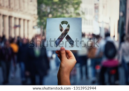 Global issue stop AIDS as hand holding a paper sheet with HIV red ribbon symbol over crowded street background. Fight against cancer concept, substance abuse and anorexia awareness.